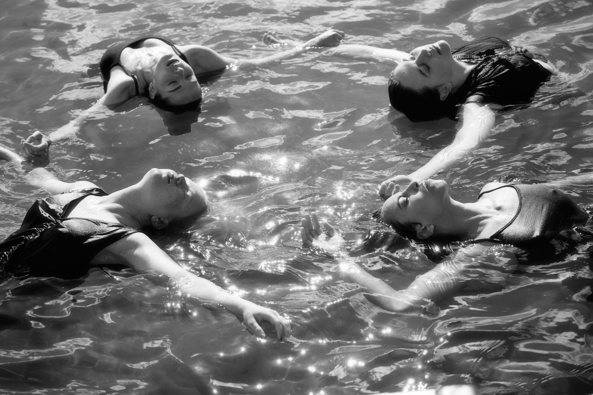 Two performers floating face-up in reflective water
