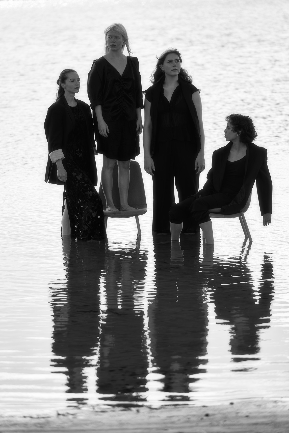 Four performers seated and standing in reflective water